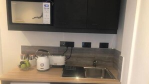 Een kleine keuken met een magnetron, broodrooster, waterkoker en spoelbak.