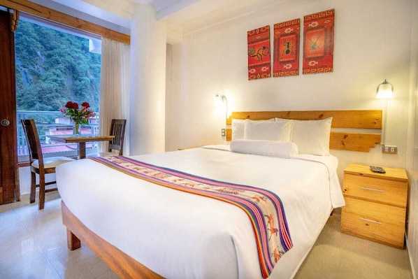 Habitación de hotel con una cama grande, cabecera de madera, mesitas de noche y vistas a un balcón con flores.