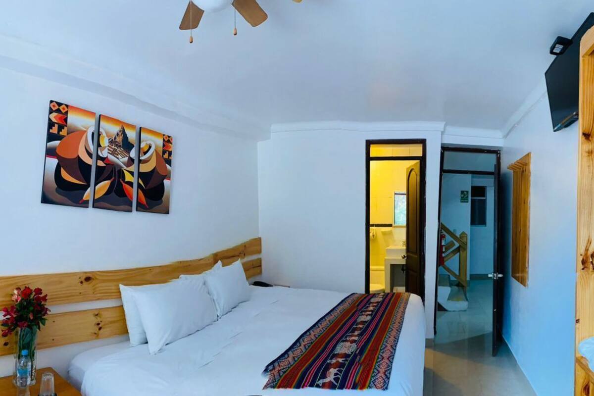Ein Schlafzimmer mit einem Holz-Kopfteil, einem Bett mit weißer Bettwäsche, einer bunten Tagesdecke, einem Bild an der Wand und einem Holzschrank mit Radio.