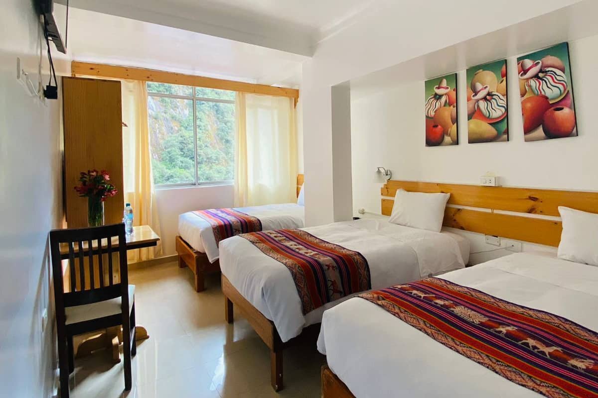 Ein Hotelzimmer mit zwei Einzelbetten, einem Holz-Kopfteil, einem Deckenventilator, einem an der Wand montierten Fernseher und einem Fenster mit Vorhängen.