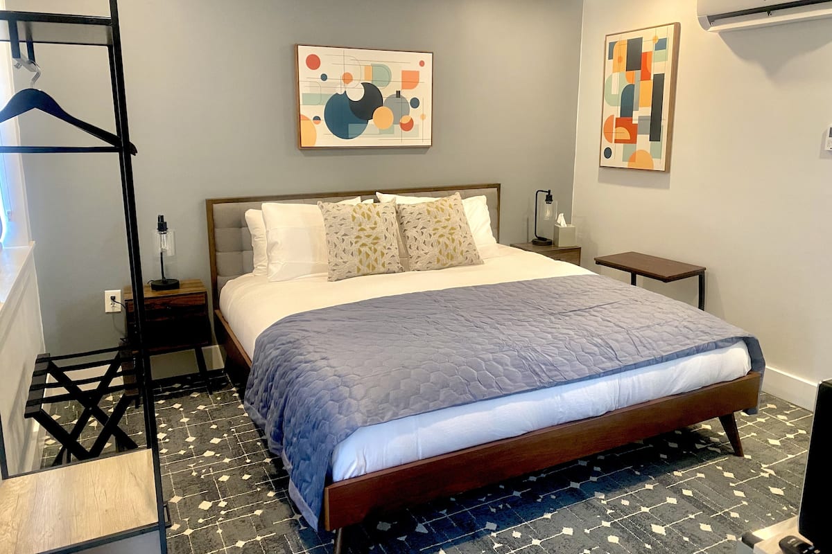 Un dormitorio ordenado con una cama, una mesita de noche, un perchero y arte abstracto en las paredes.
