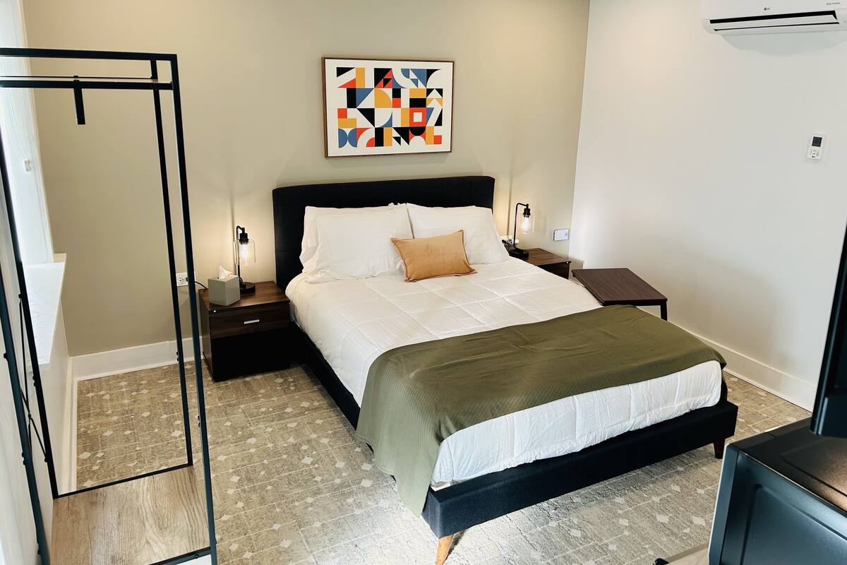 Un dormitorio moderno con cama, mesitas de noche, una lámpara y un cuadro en la pared.