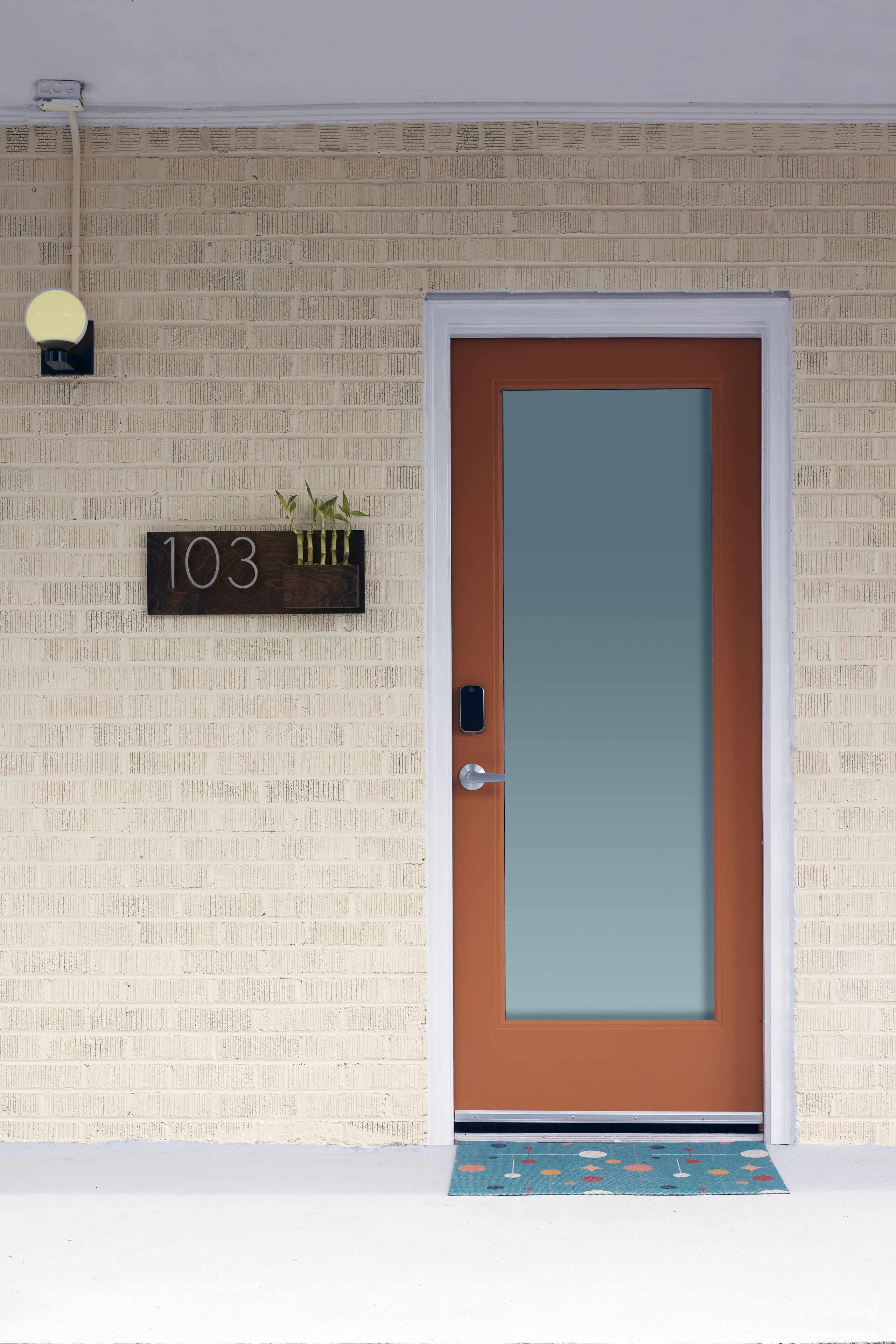 A door with a number sign above it, a doormat, and a wall with newspaper clippings.