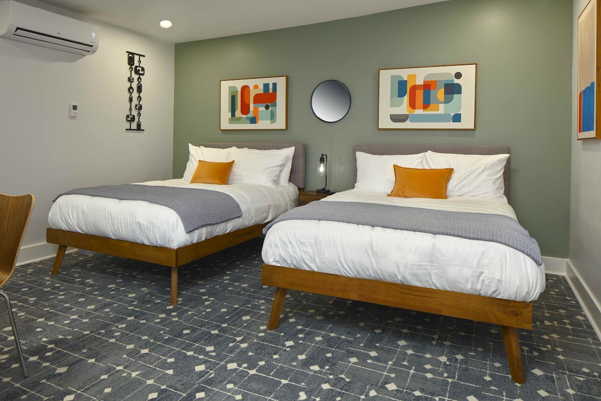 Habitación de hotel con dos camas individuales, suelo de madera y aire acondicionado instalado en la pared.