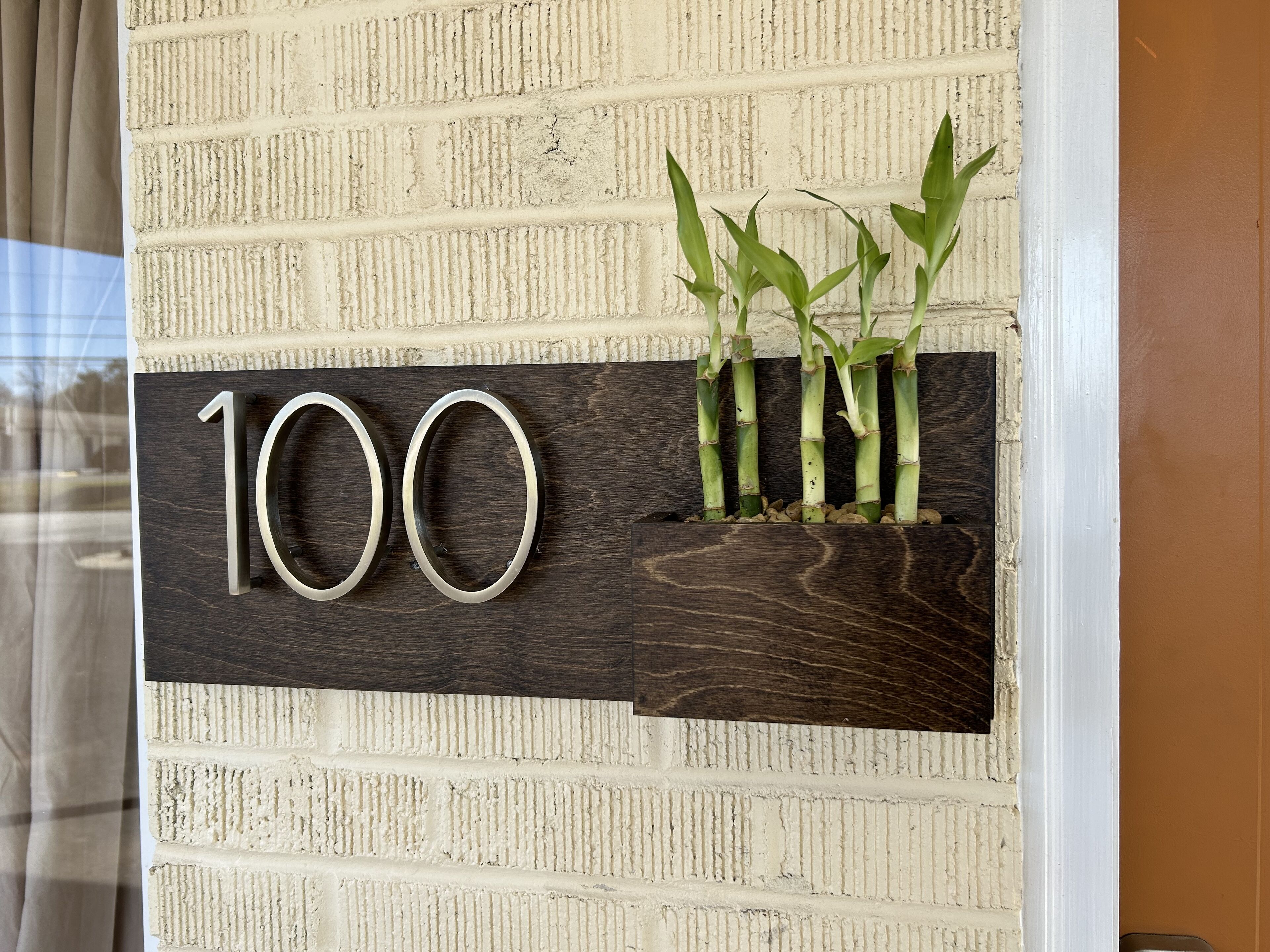 A house number sign with a wooden background and three bamboo plants.