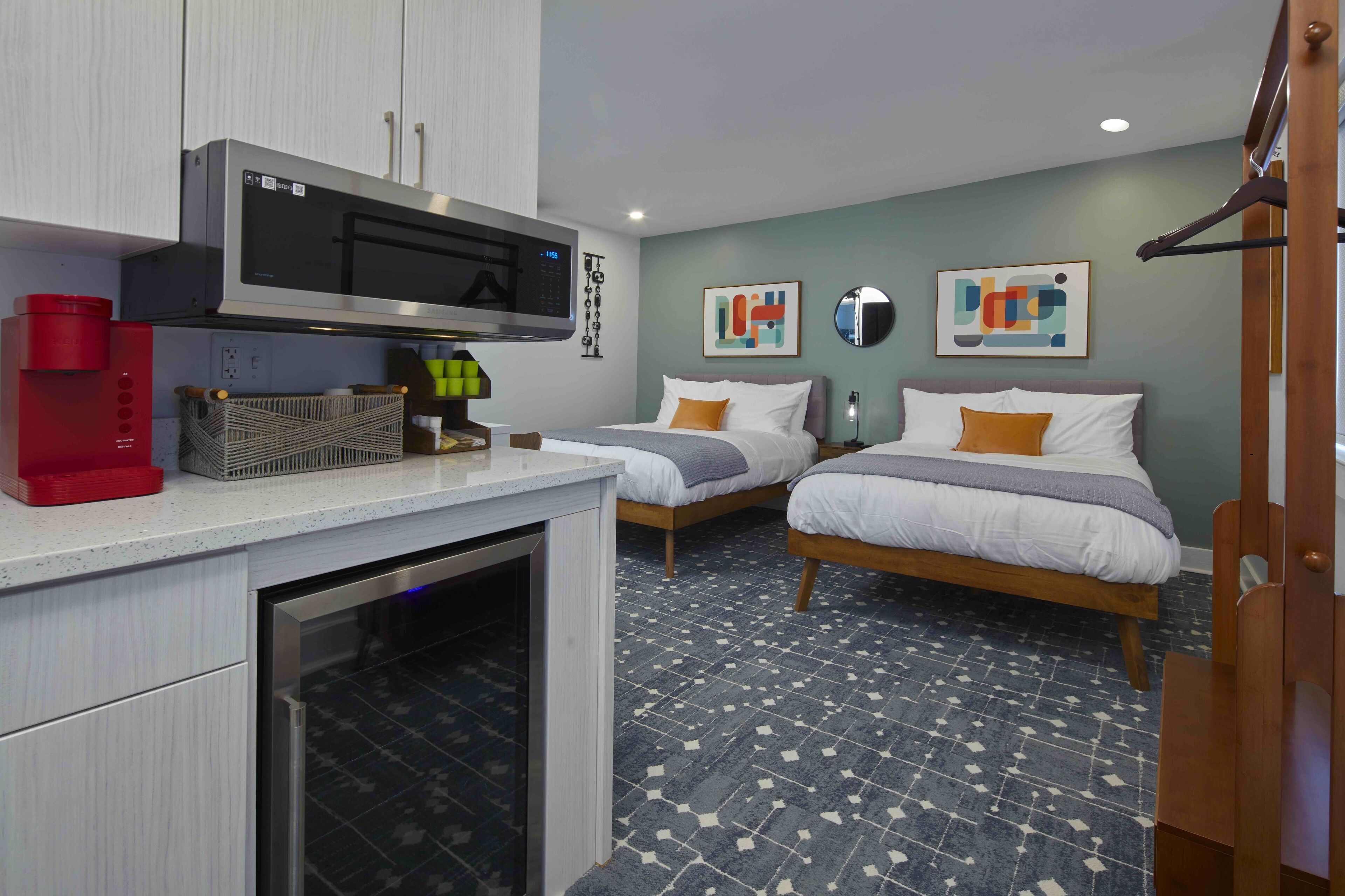 A hotel room with two beds, a kitchenette, and a bathroom.