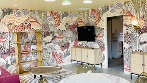 A dining area with a round table, chairs, a television, and a patterned wall. - New South Motor Inn (Madison)