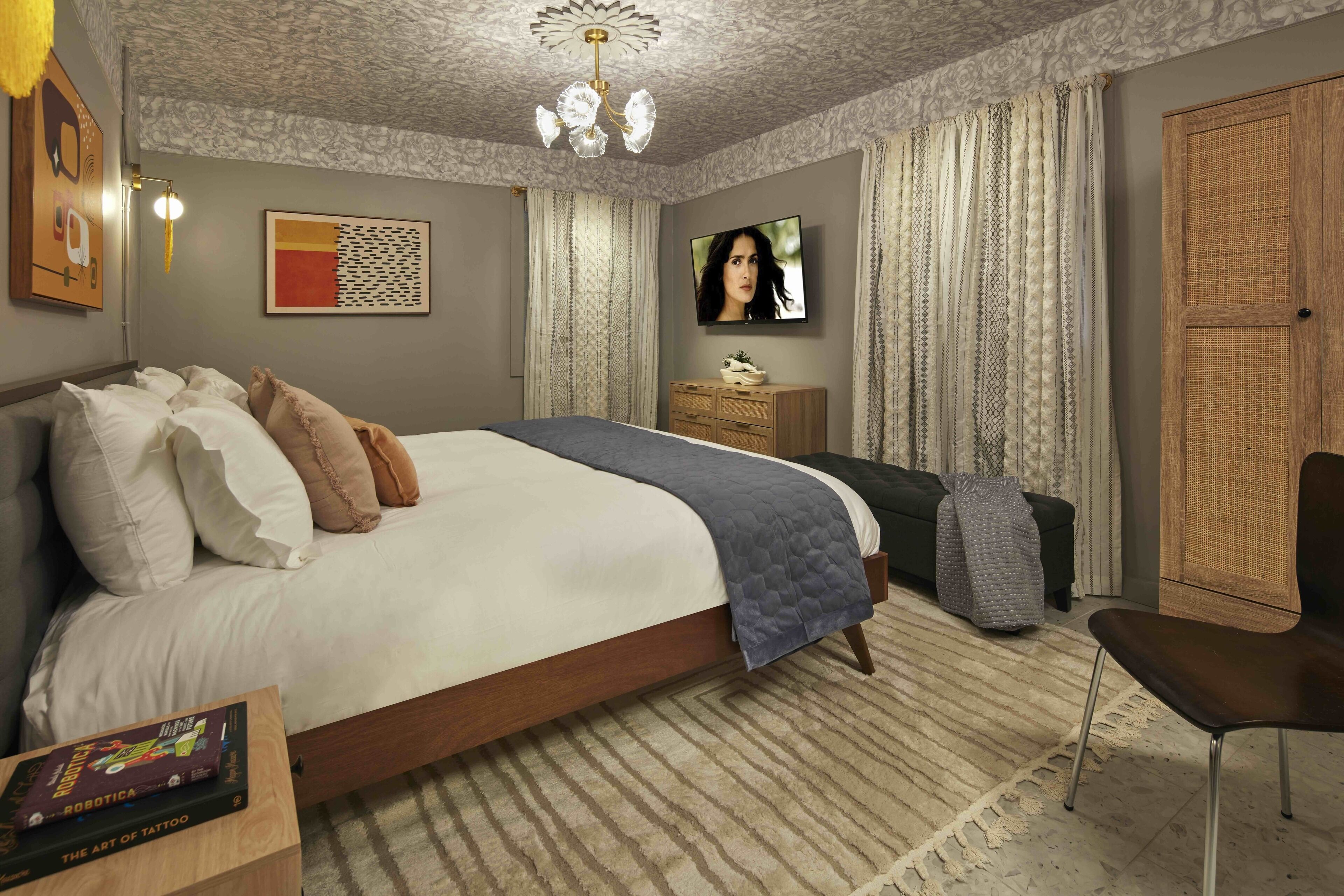 A bedroom with a large bed, a flat-screen TV, a wooden wardrobe, and a small table with a book.