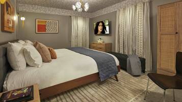 A bedroom with a large bed, a flat-screen TV, a wooden wardrobe, and a small table with a book.