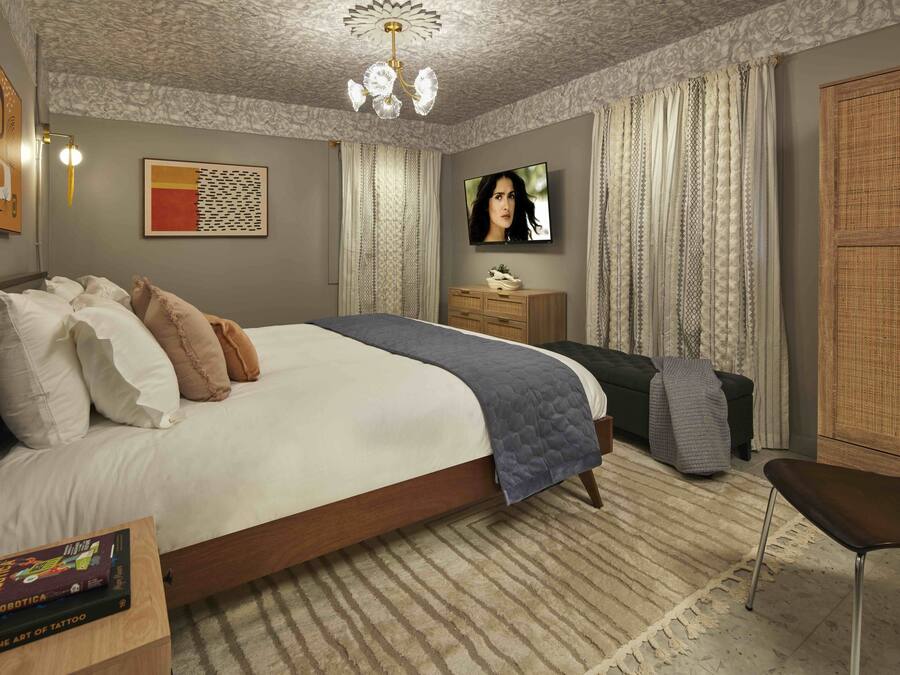 A bedroom with a large bed, a flat-screen TV, a wooden wardrobe, and a small table with a book.