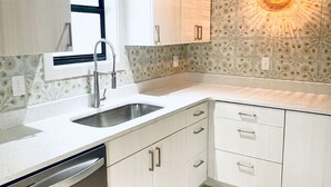 A kitchen with white cabinets, a stainless steel sink, and a patterned backsplash. - New South Motor Inn (Madison)