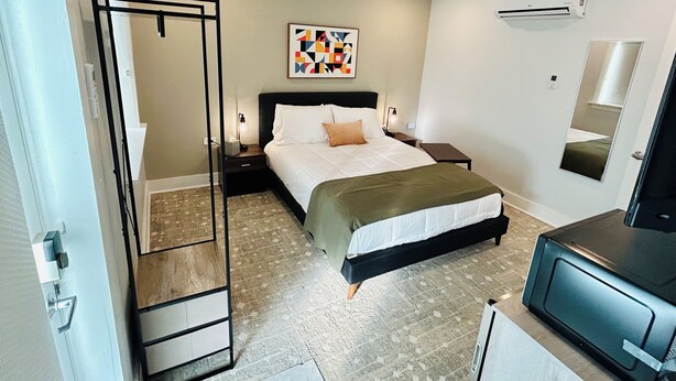 A hotel room with a bed, bedside tables, an air conditioner, a mirror, and a TV. - New South Motor Inn (Madison)