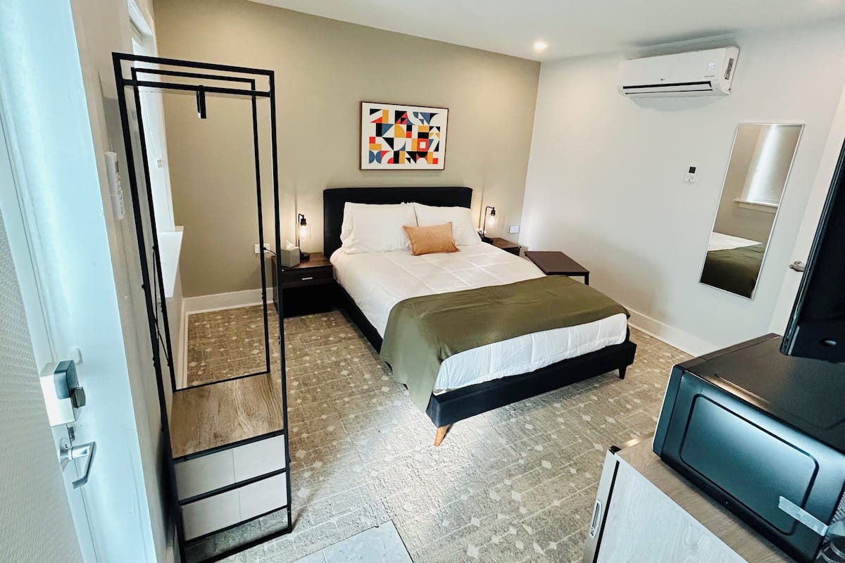 Una habitación de hotel con cama, mesitas de noche, aire acondicionado, espejo y televisor.