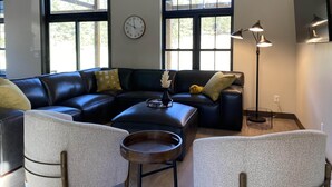 A modern living room with a sectional sofa, two armchairs, a coffee table, and a floor lamp. There are large windows providing natural light and a clock on the wall. - Custer's Retreat - 2 BD Cabin (Custer)