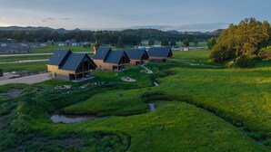A row of modern cabins with sloped roofs, set in a lush green landscape with a small stream. - Custer's Retreat - 2 BD Cabin (Custer)