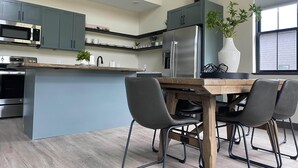 A modern kitchen with grey cabinets, stainless steel appliances, a wooden island with a black chair, and a potted plant. - Custer's Retreat - 2 BD Cabin (Custer)