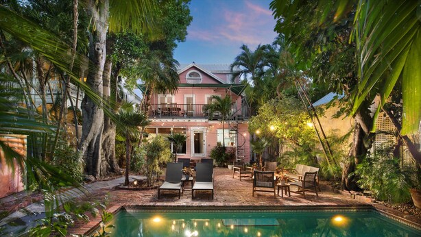 A pool area with lounge chairs and a dining table, surrounded by lush tropical plants. - 3 Bedroom Home - Perfect Location & Private Pool (Key West)