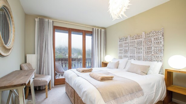 Ein Schlafzimmer mit einem großen Bett, einem Schreibtisch, einem Stuhl und Blick ins Freie.