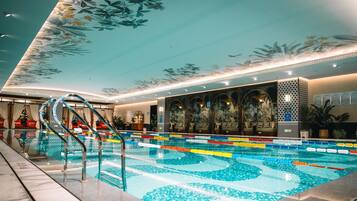 Une piscine intérieure avec des couloirs bien délimités, un sol carrelé et une fresque murale au plafond.
