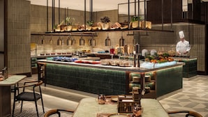 Una cocina moderna con una isla central, taburetes de bar y un chef preparando comida.