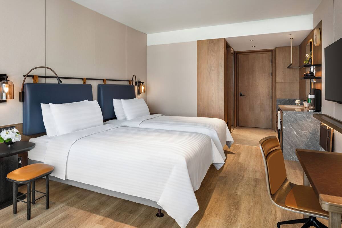Une chambre d’hôtel moderne équipée de deux lits, d’un bureau et d’une petite kitchenette.