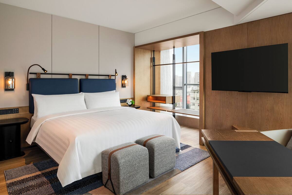 Une chambre d’hôtel moderne avec un grand lit, un bureau et un téléviseur fixé au mur.