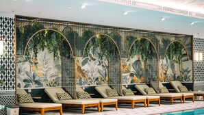 Zona de piscina con sillones de descanso y un muro decorativo con motivos vegetales.
