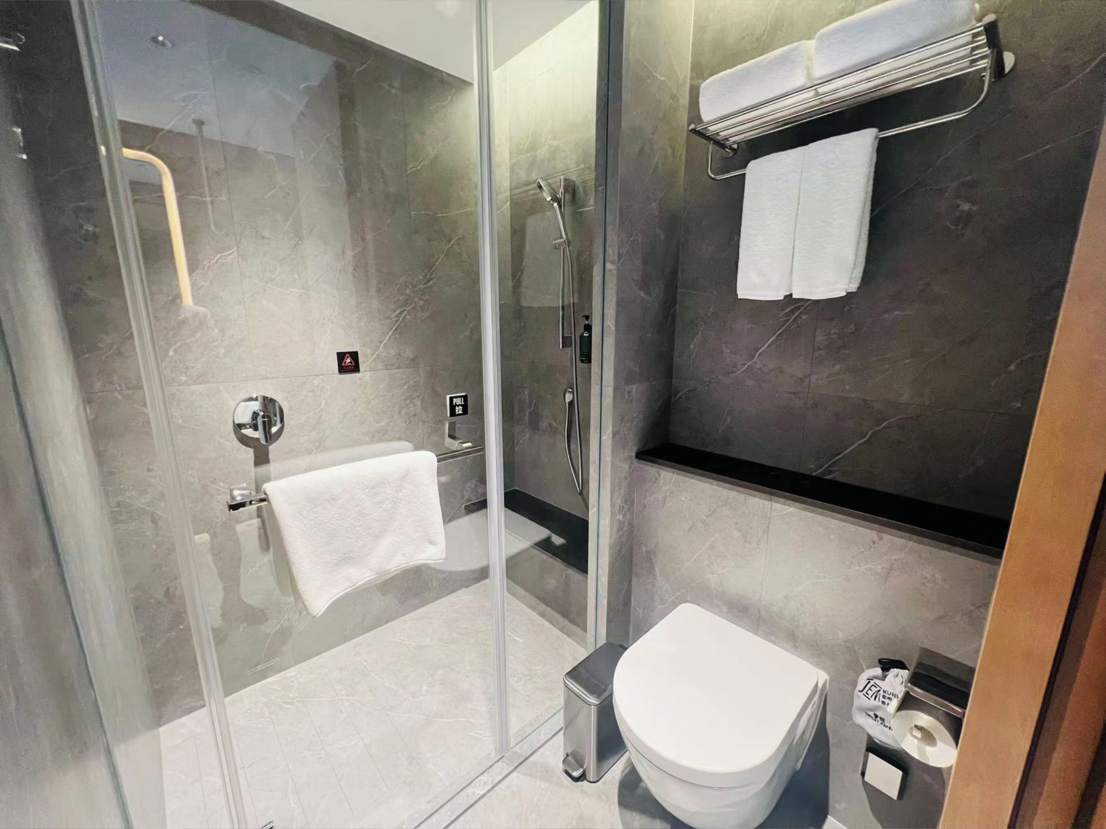 A modern bathroom with a glass-enclosed shower, a toilet, and a towel rack.
