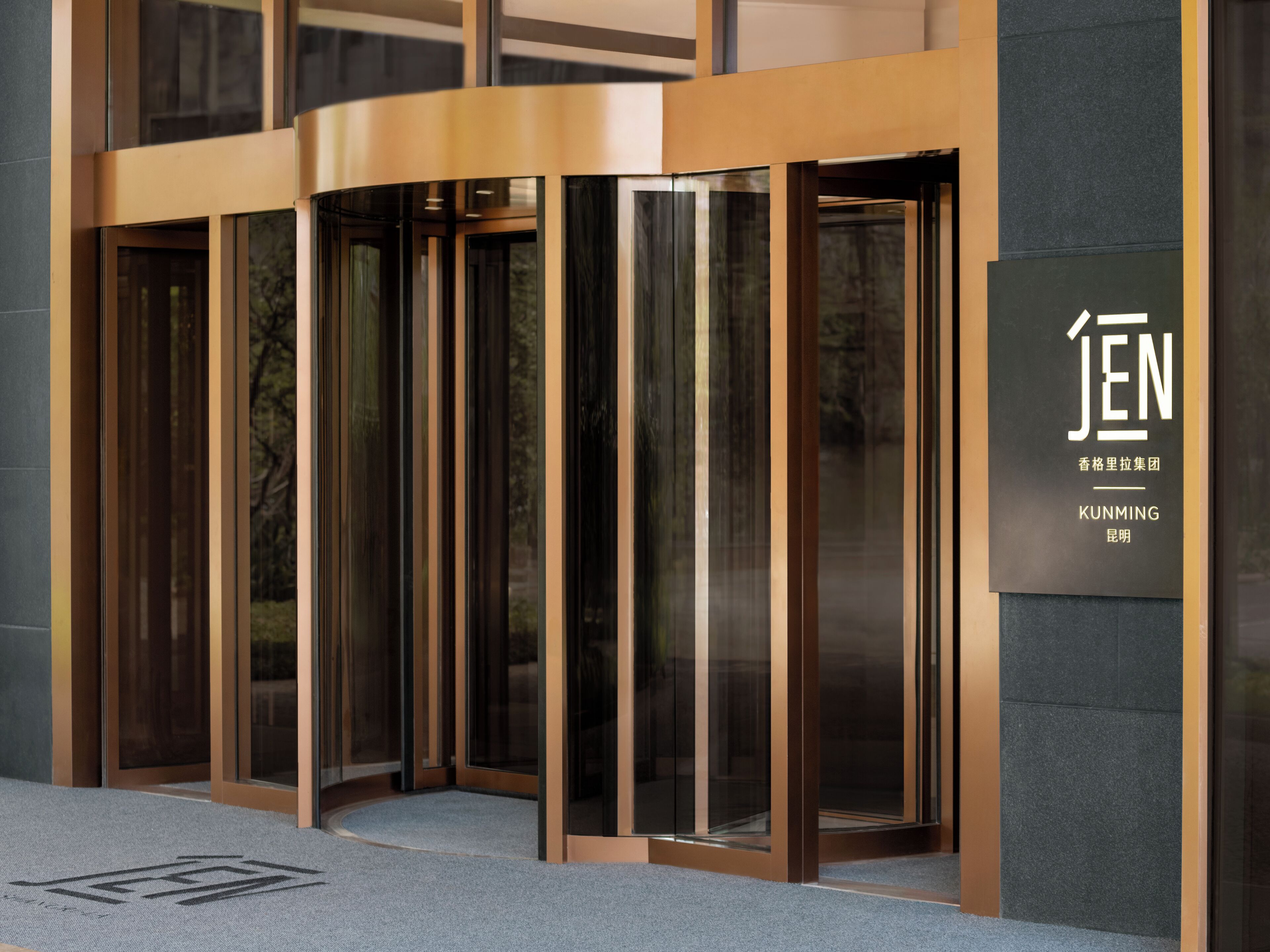 Entrada moderna de un edificio con puertas giratorias de vidrio y un letrero que indica el nombre JEN.