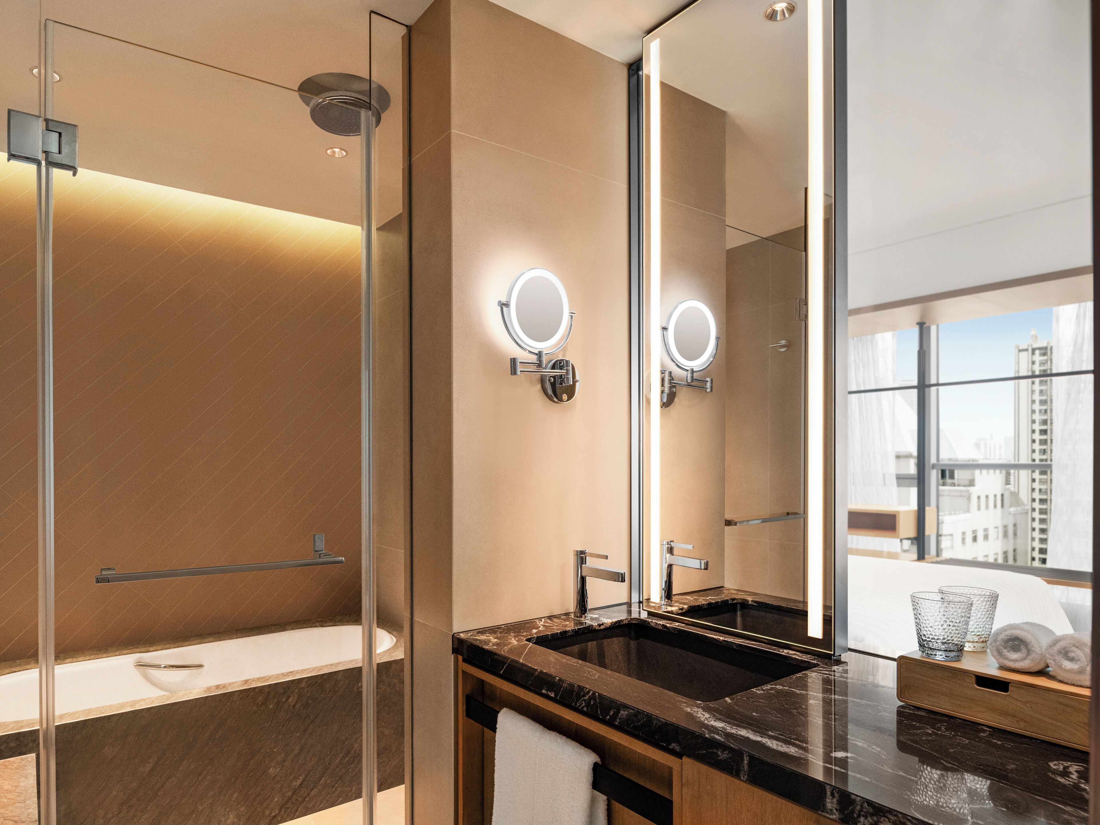 A modern bathroom with a glass shower enclosure, a bathtub, a vanity with a black marble countertop, and a large mirror with wall-mounted lights.