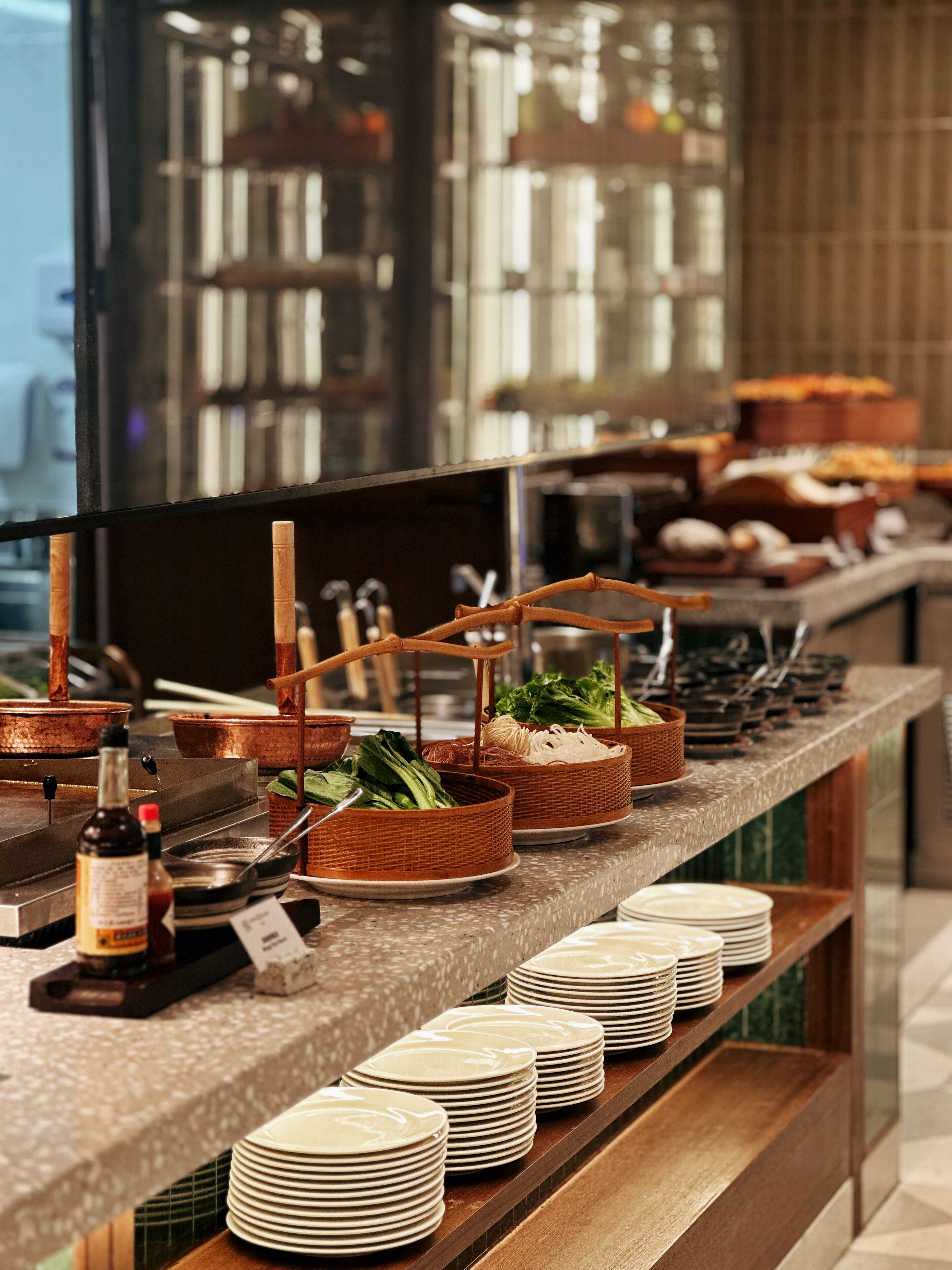 Un buffet avec différents plats présentés dans des paniers et sur des assiettes, une bouteille de sauce et une pile d’assiettes.