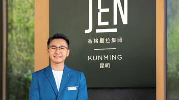 A man in a blue suit standing in front of a sign with the word "JEN" and some Chinese characters.