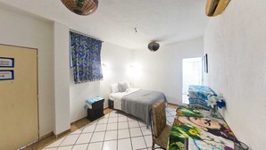 Une petite pièce propre, avec un lit, une table et une chaise. Il y a une fenêtre avec des rideaux, une porte et un globe terrestre fixé au mur.