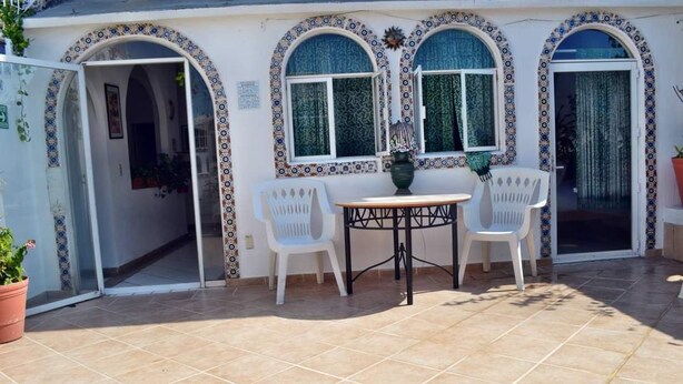 Un espace patio aménagé avec une table et des chaises, un pot de fleurs et une porte donnant sur un espace intérieur.