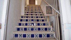 Un escalier dont les marches sont recouvertes de carreaux aux motifs bleus et blancs, avec des rampes blanches et un mur uni.