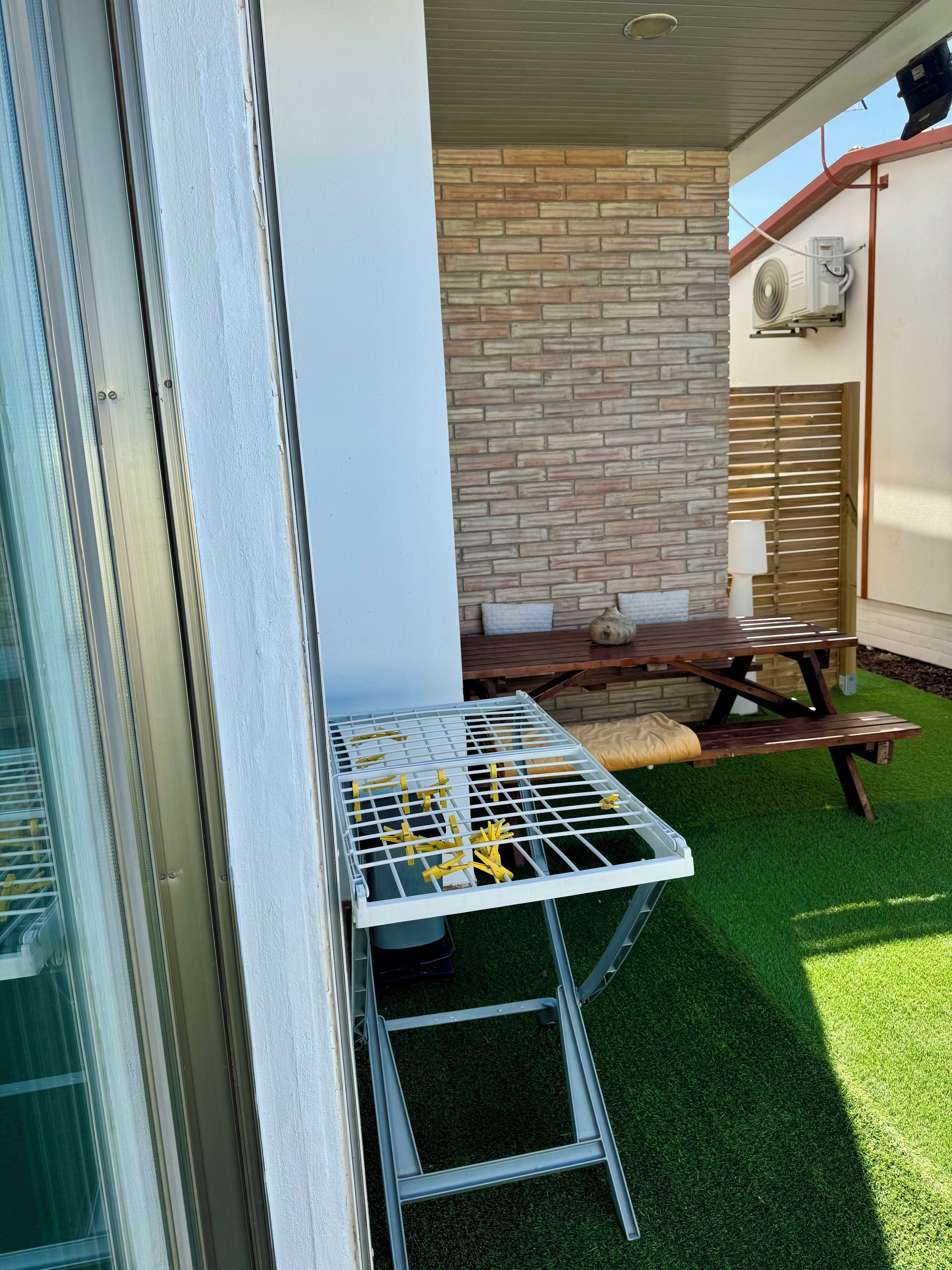 Uma área de pátio com mesa e cadeiras, um muro de tijolos e um aparelho de ar condicionado.