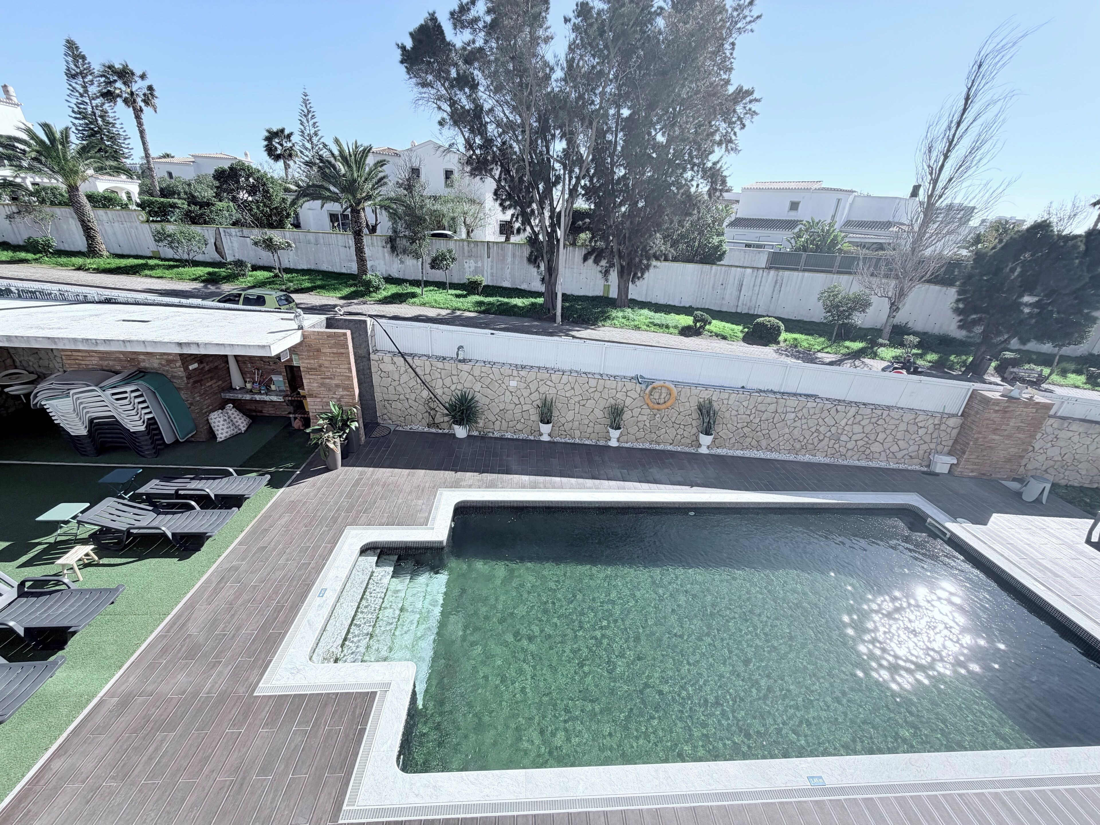 A swimming pool with a stone wall and a patio area with lounge chairs.