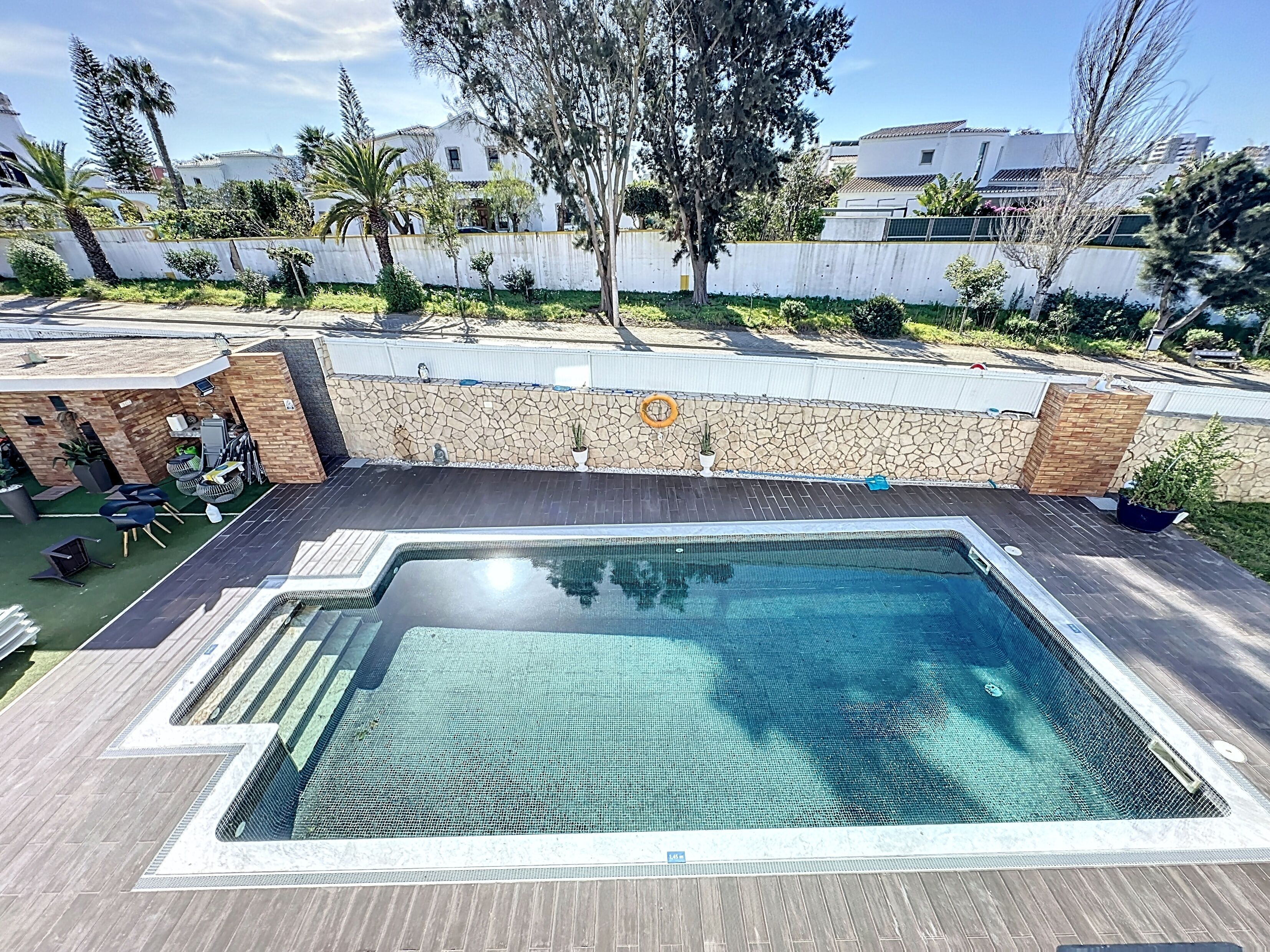 Piscina retangular ao ar livre com parede de pedra e deck de madeira ao redor.