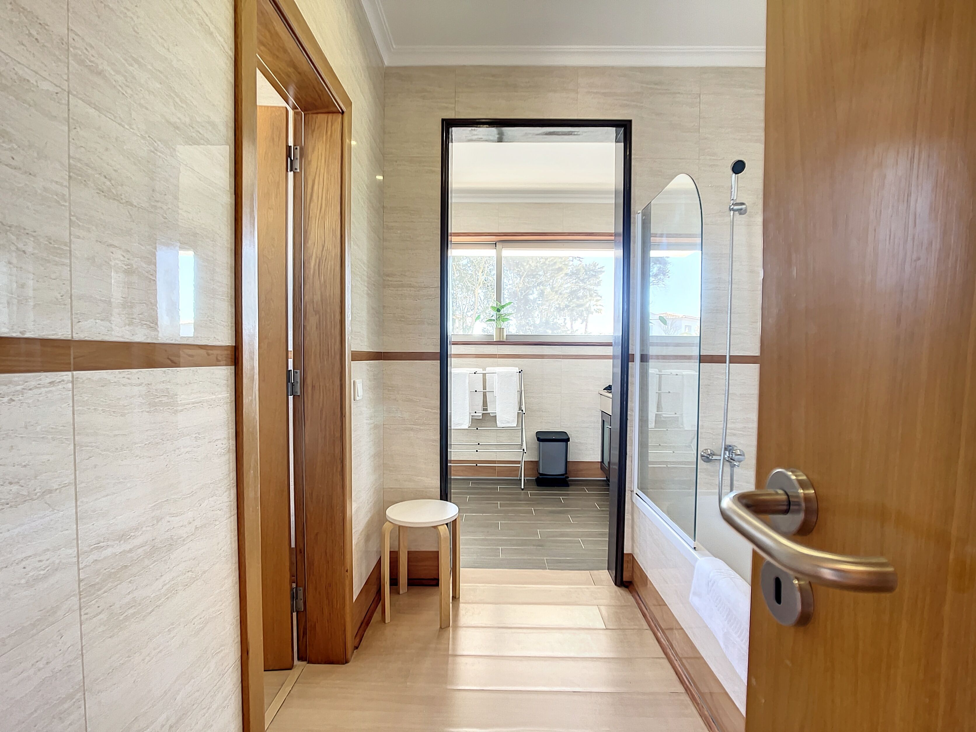 Un baño moderno con ducha de vidrio, un taburete de madera y vistas al exterior.
