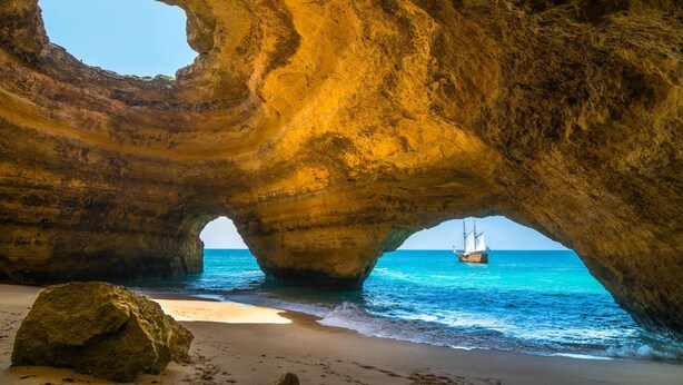 Una formazione rocciosa naturale con un'apertura simile a una grotta, una spiaggia sabbiosa e una barca a vela nell'acqua.