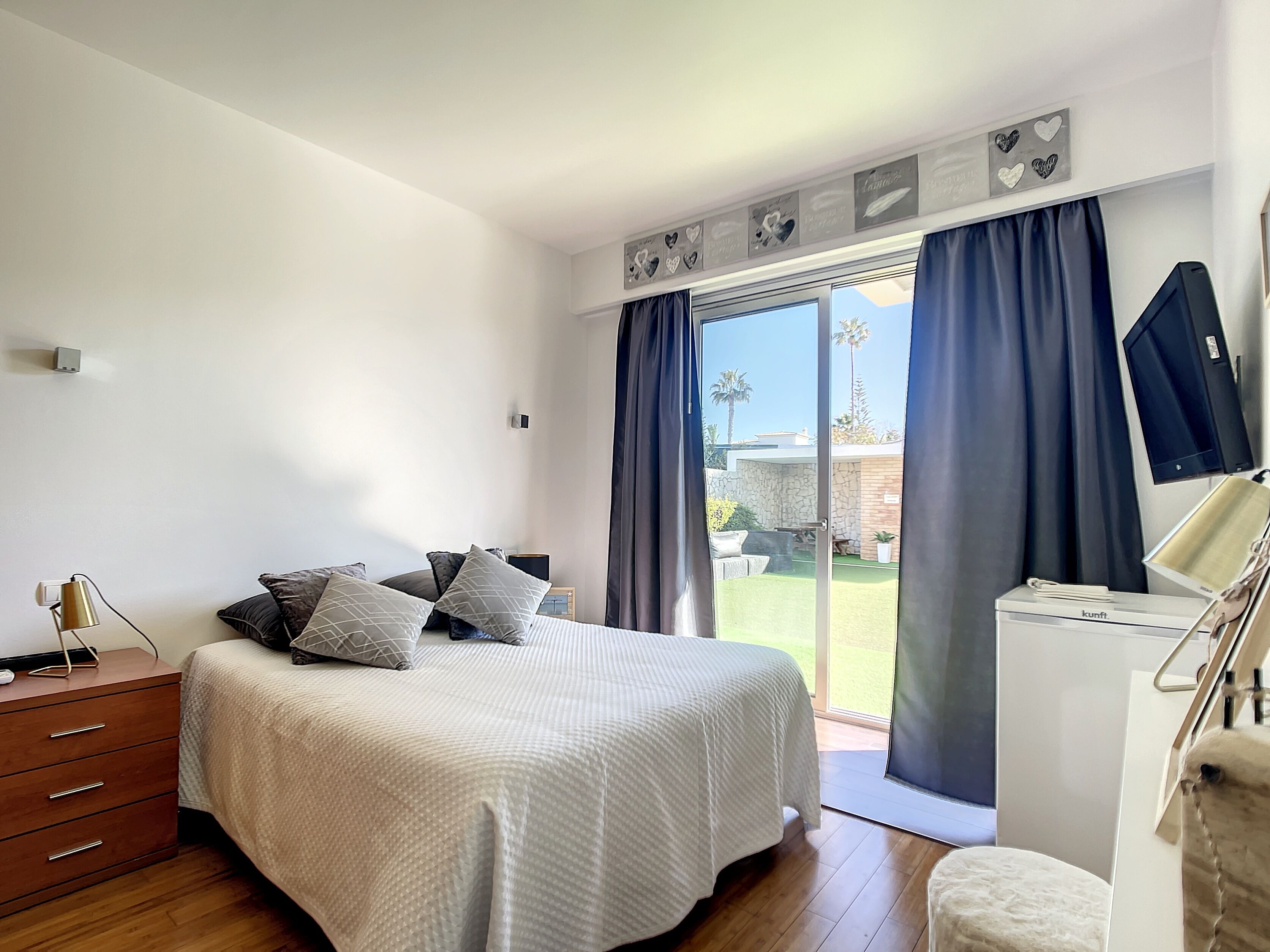 A bedroom with a bed, a dresser, a desk, and a sliding glass door leading to an outdoor area.