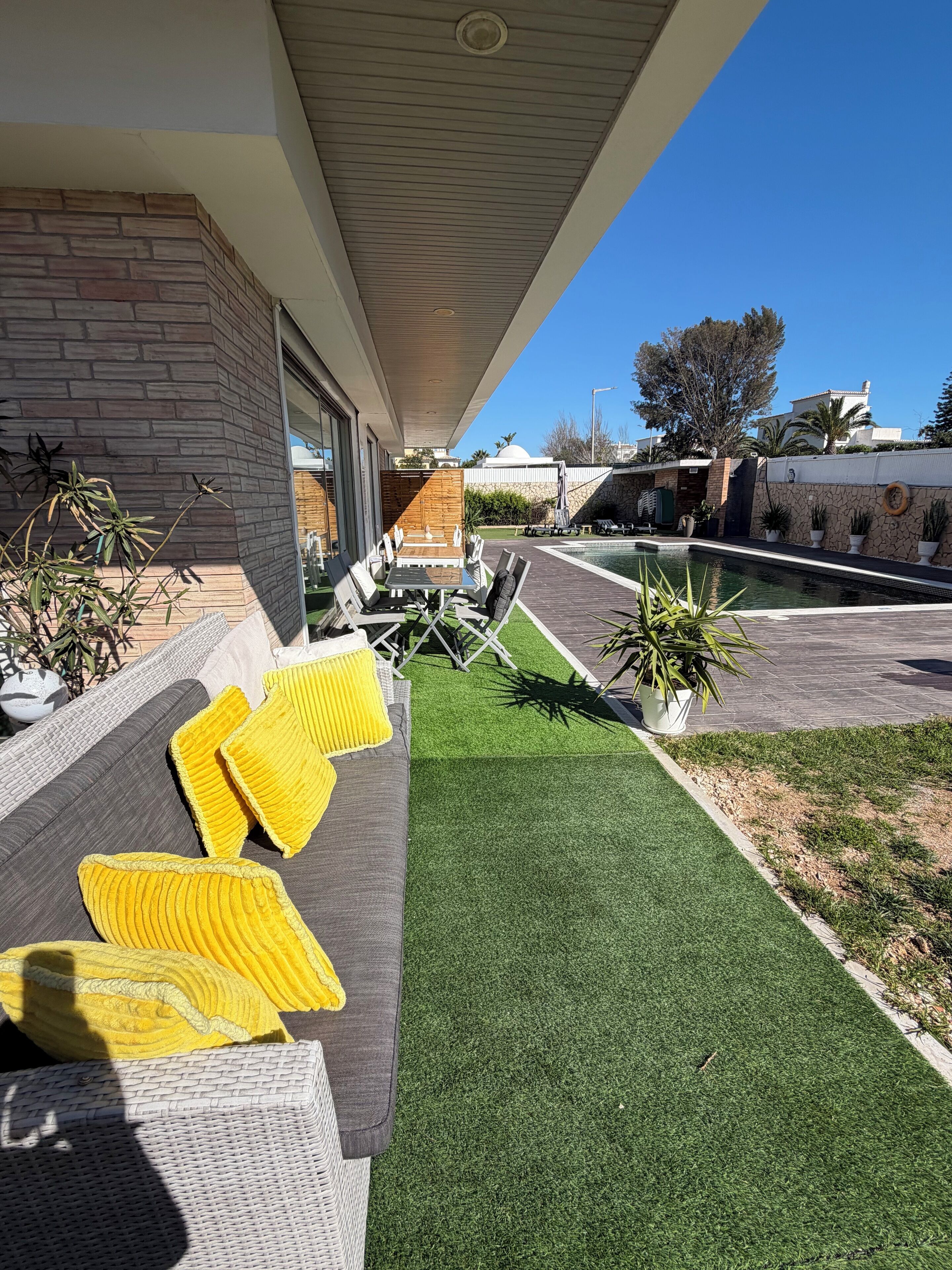 Un patio moderno al aire libre con piscina, césped artificial y mobiliario exterior.