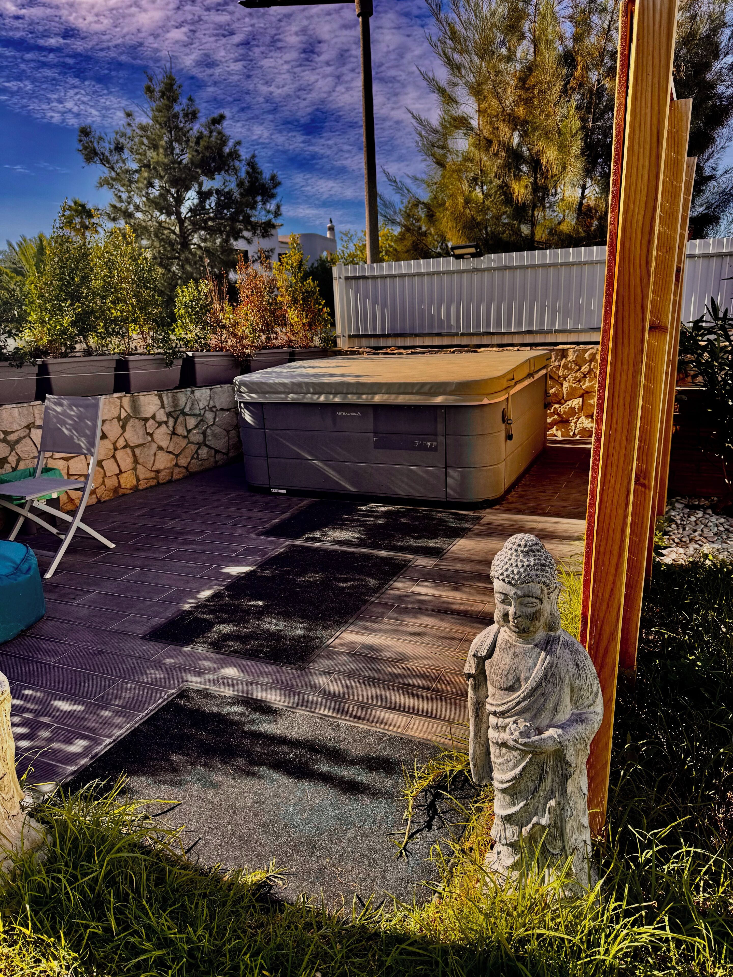 A garden with a hot tub, stone wall, and a Buddha statue.