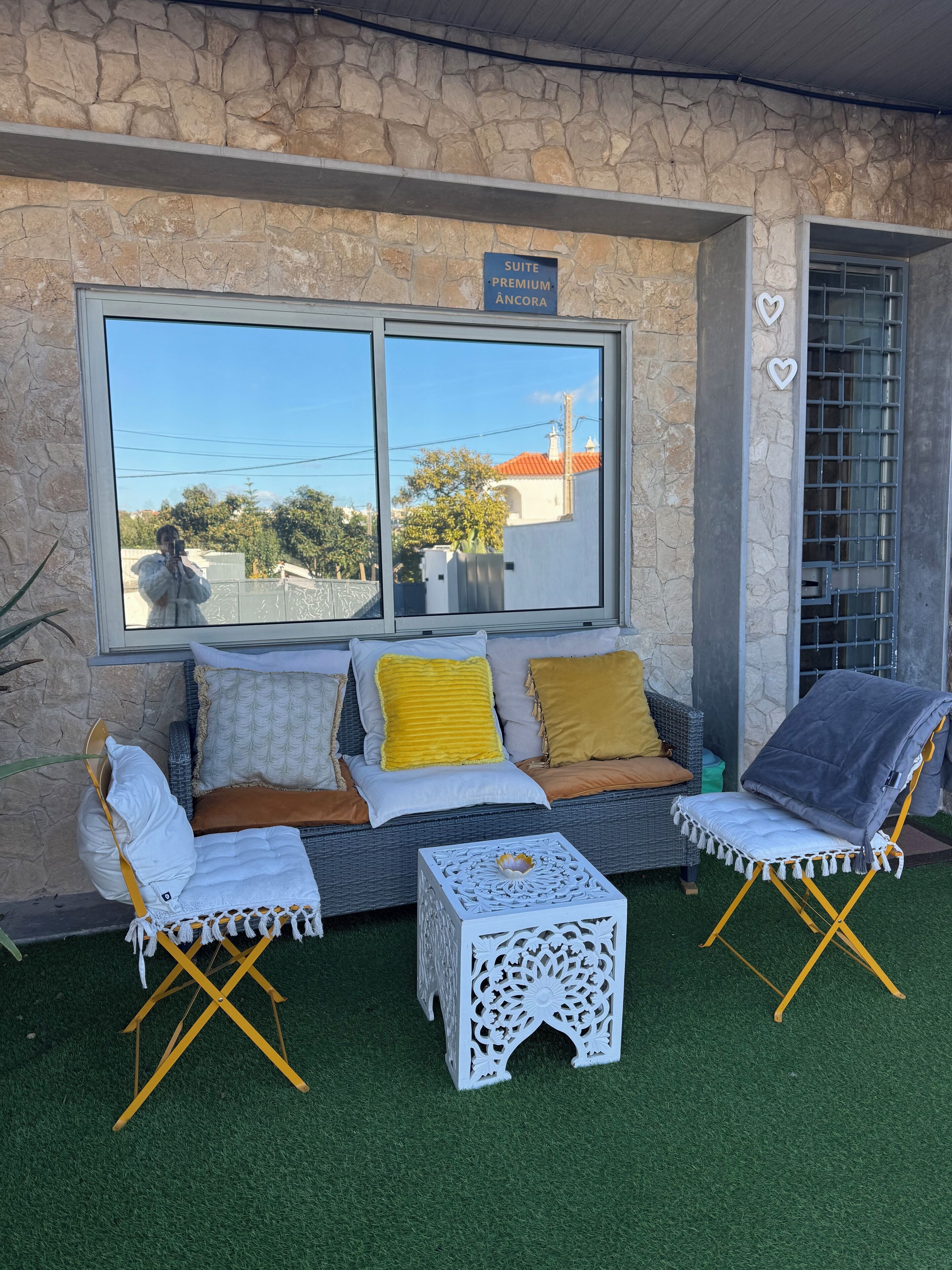 A cozy outdoor seating area with a stone wall, a large window, and a sign indicating a 'Suite Premium Ancora'.