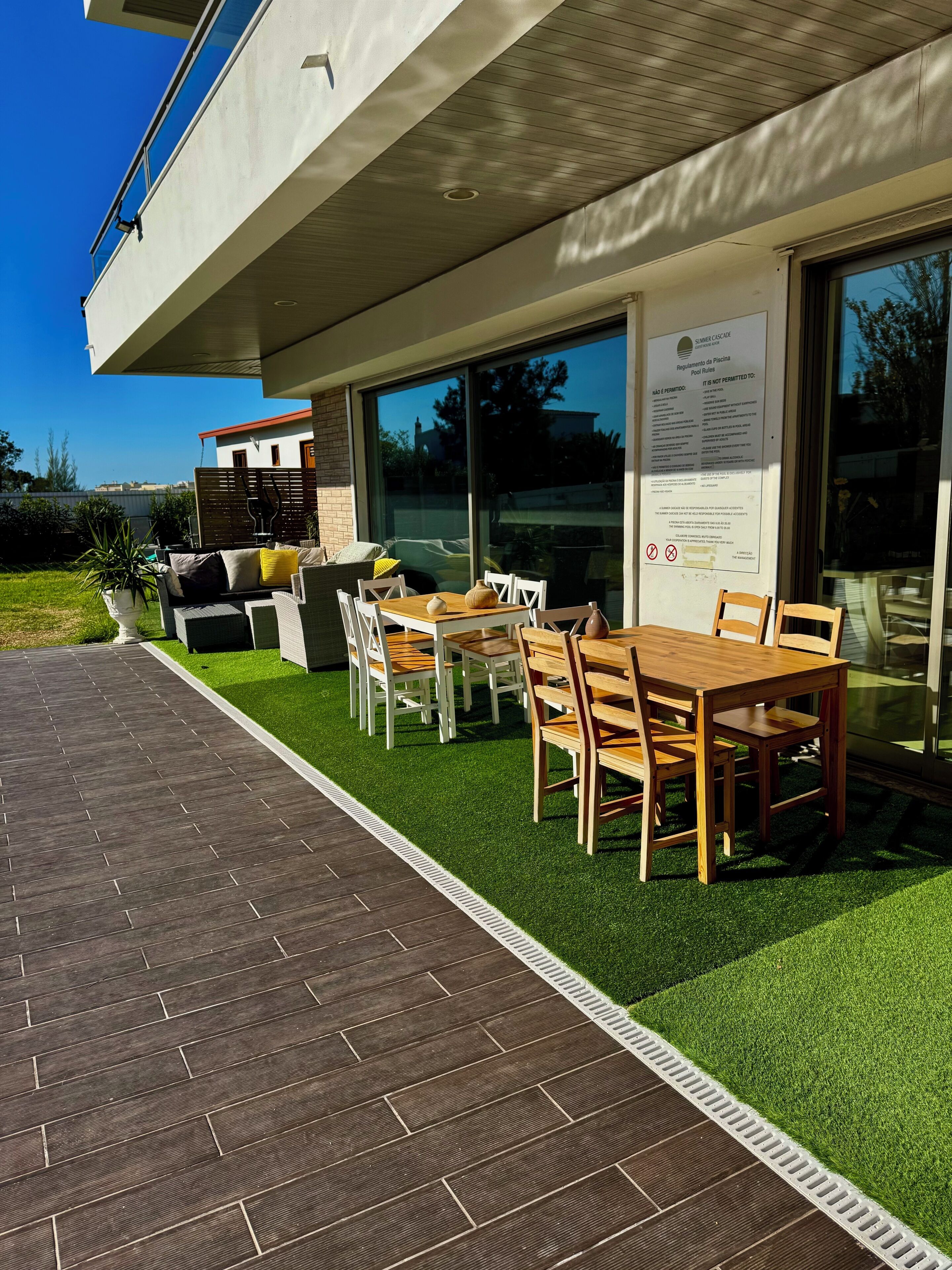 Un espace extérieur aménagé en terrasse, avec une table et des chaises, un pot de fleurs et un panneau fixé au mur.