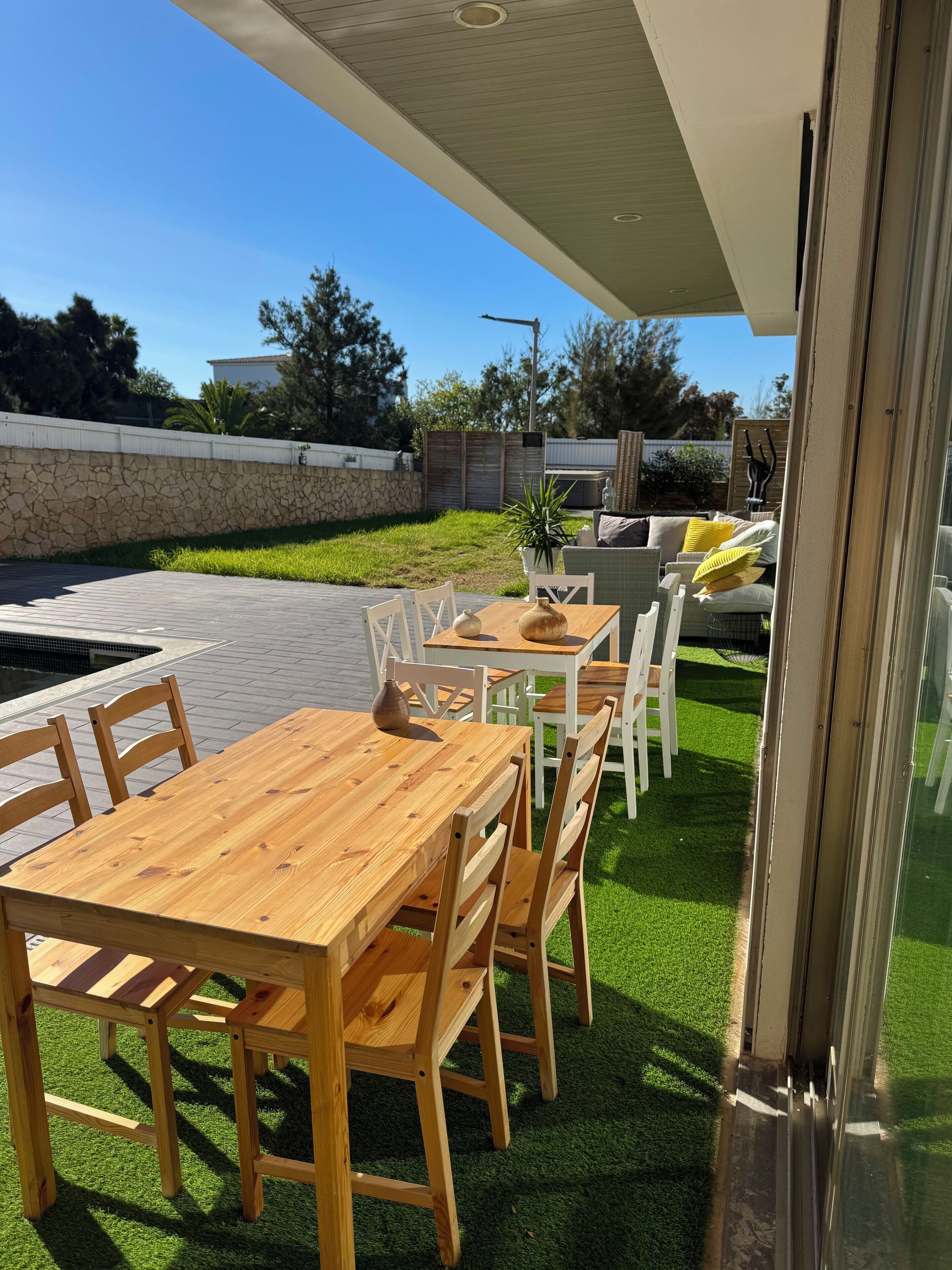 Eine Terrasse im Freien mit einem Holztisch und -stühlen, einem kleinen Topfpflanzen und einer Sitzgruppe mit Kissen.