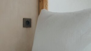 Een hoek van een kamer met een wit kussen en een klein, donker vierkant object aan de muur.