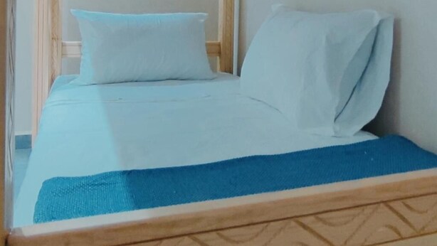 Een bed met een blauwe spreideken en witte kussens in een kamer met een houten hoofdbord en een raam.