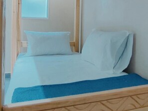 A bed with a blue bedspread and white pillows in a room with wooden headboard and a window. - Mixed Dormitory Room - Surf Camp Tamraght (Aourir)