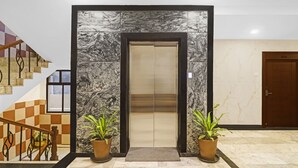 A modern elevator entrance with marble walls, a wooden staircase to the left, and a door to the right. - SYN Elite Residency (Hyderabad)